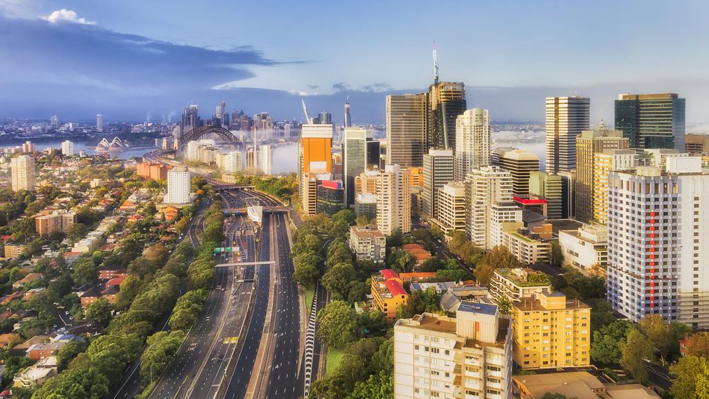 North Sydney CBD in aerial view over motorway leading to the Sydney Harbour bridge, harbour and city at sunrise with foggy weather.