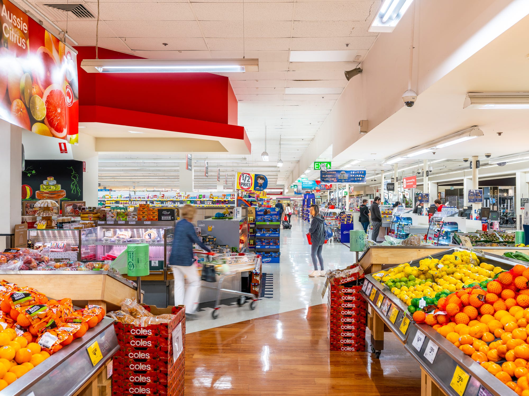 Inside a Coles supermarket, with fruit on display, the deli and shoppers in the aisles.