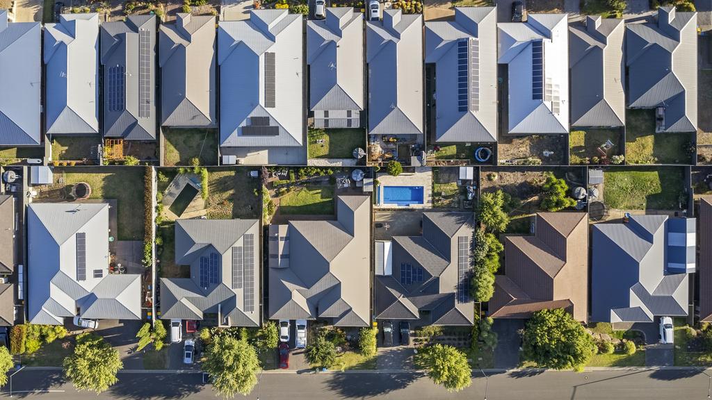 Aerial view directly above new rural housing development, mostly grey roofing, some green landscaping, trees, orange-coloured street trees.