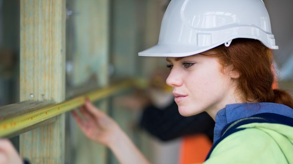 Young woman carpenter on building site measuring with tape measure