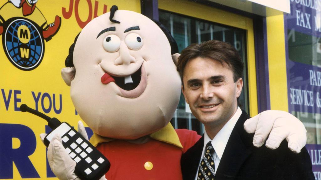 Owner and businessman John Ilhan with mascot for his Crazy John's Telstra MobileNet mobile phone dealerships, outside one of his stores in Melbourne, 27/10/98.